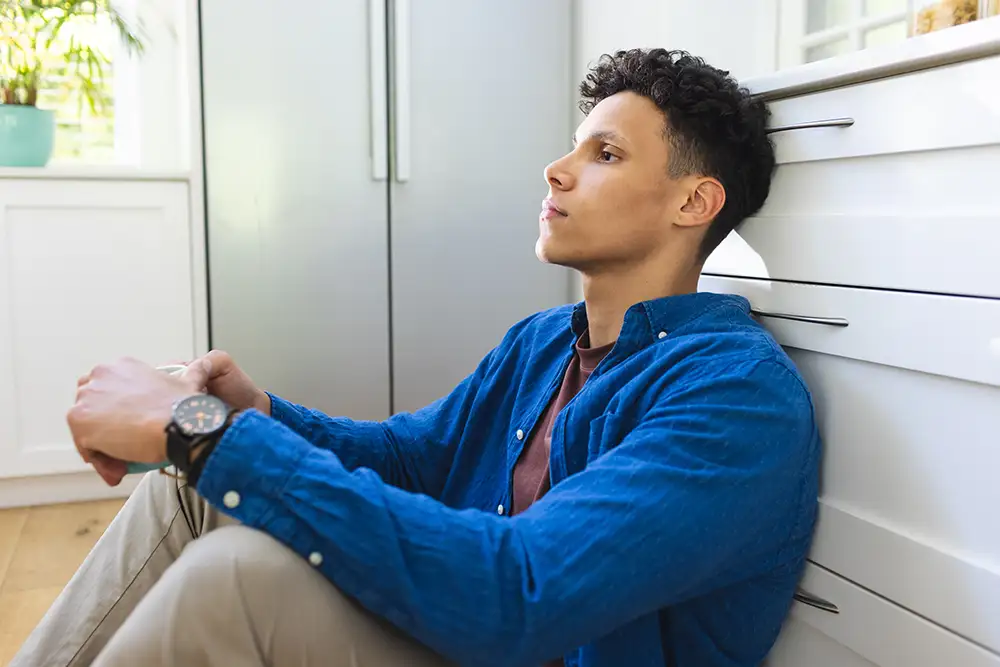 Concerned biracial man sitting on floor and holding tea cup